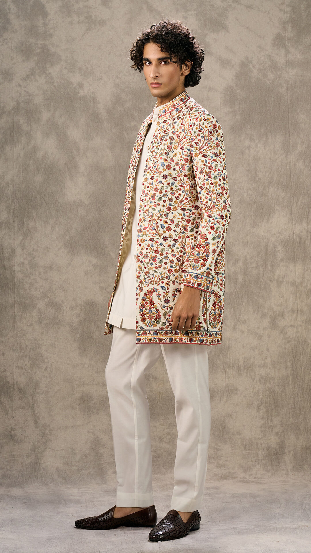 Stylish man wearing a cream kurta set paired with an intricately embroidered floral sherwani jacket, traditional ethnic fashion for weddings and festive occasions.